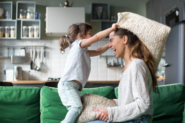 Photo of a child having pillow fight with adult woman.