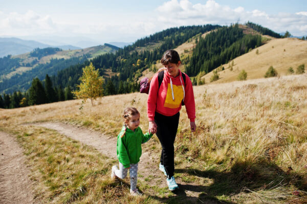Photo of an adult woman with dark hair, walking along an outdoor hiking trail with a little blonde haired girl next to her.